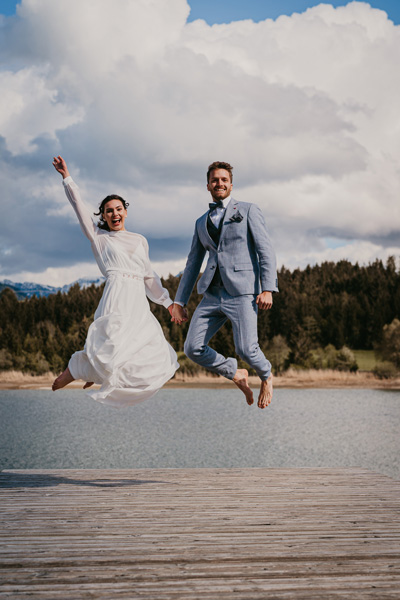 Freudensprung von Braut und Bräutigam nach ihrer Bergsee-Hochzeit